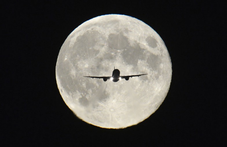 A passenger aircraft, with the full "Harvest Moon" seen behind, makes its final approach to landing at Heathrow Airport in west London
