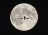 A passenger aircraft, with the full "Harvest Moon" seen behind, makes its final approach to landing at Heathrow Airport in west London